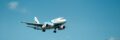 A passenger airplane descends for landing over lush hills in sunny Thailand.